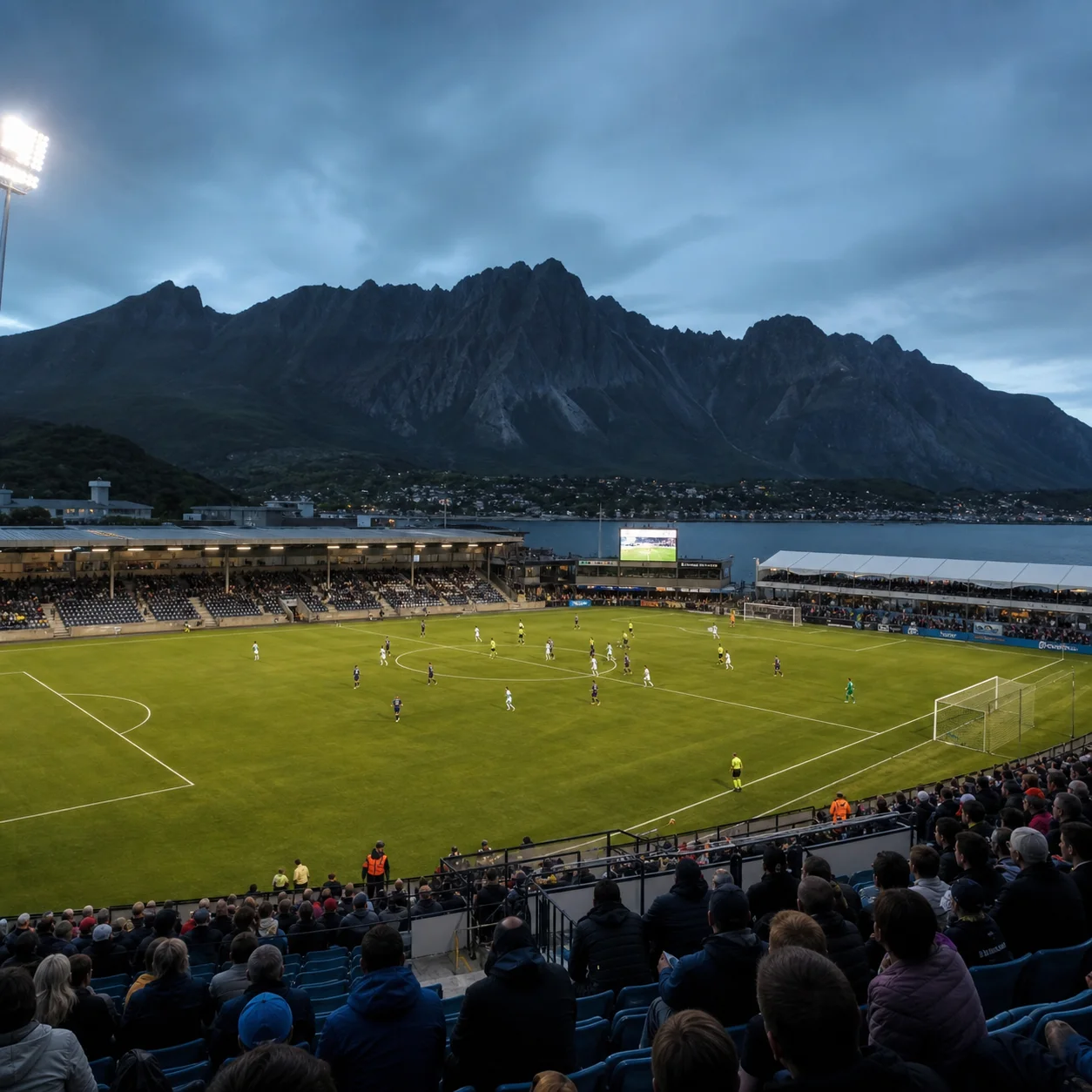 Fotbollsarena i kvällsljus med publik runt planen.
