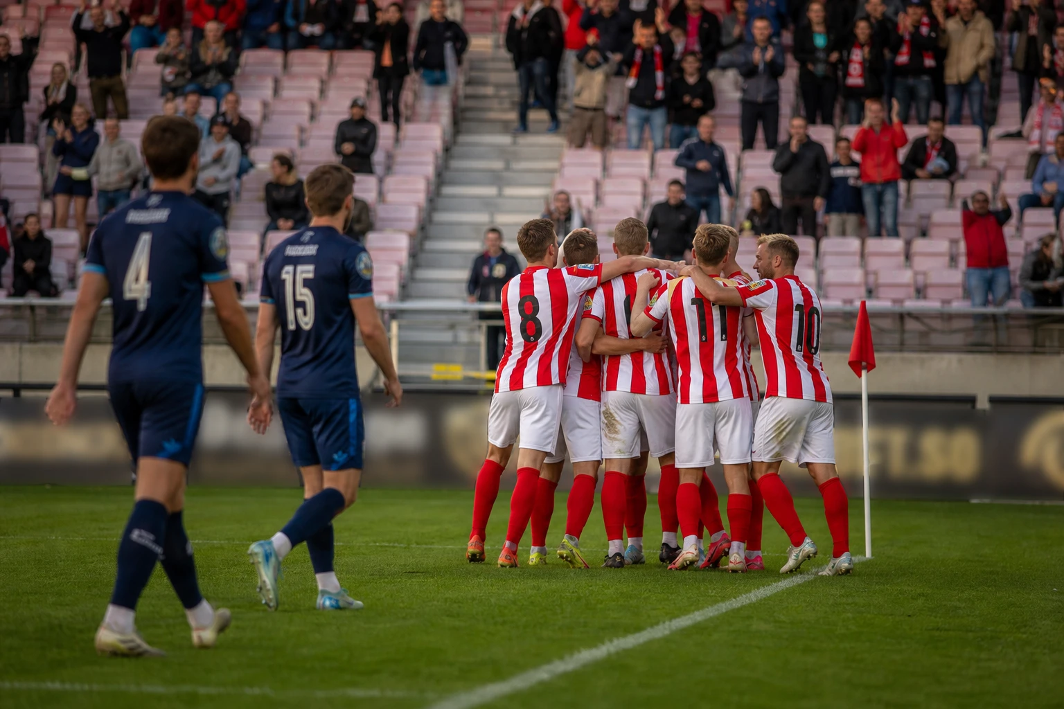 Spelare i randiga tröjor samlas i måljubel framför huvudläktaren.